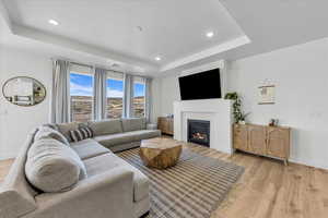 Living room featuring a glass covered fireplace, baseboards, light wood-type flooring, recessed lighting, and a raised ceiling