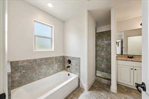 Full bathroom with a bath, tiled shower, vanity, and baseboards