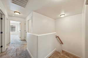 Corridor with visible vents, an upstairs landing, a textured ceiling, and light colored carpet