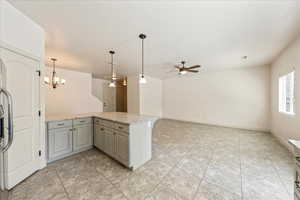 Kitchen featuring gray cabinetry, light tile patterned flooring, light stone countertops, a peninsula, and ceiling fan with notable chandelier