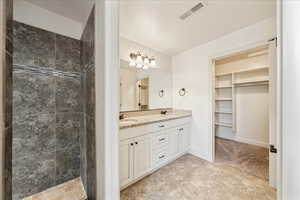 Full bath featuring double vanity, visible vents, tiled shower, and a sink