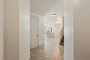 Corridor with light tile patterned floors, stairs, a notable chandelier, and baseboards
