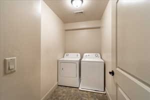 Clothes washing area with a textured ceiling, independent washer and dryer, visible vents, baseboards, and laundry area