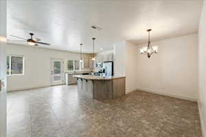Kitchen featuring light stone countertops, stainless steel appliances, ceiling fan with notable chandelier, baseboards, and visible vents