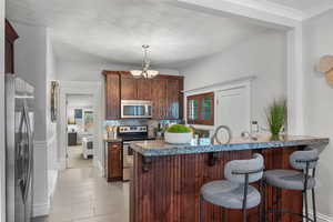 Kitchen featuring stainless steel appliances, a kitchen bar, a chandelier, decorative backsplash, and hanging light fixtures