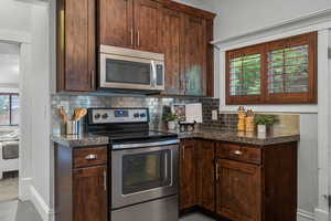 Kitchen featuring appliances with stainless steel finishes, backsplash, and dark countertops