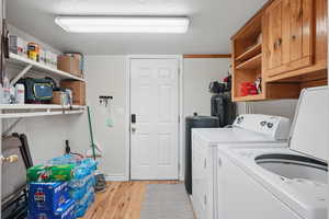 Washroom with washer and dryer, light wood-style floors, and cabinet space