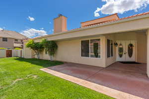 Back of house with a chimney, a patio, stucco siding, and a lawn