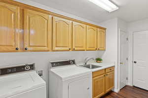 Laundry area with washer and dryer, a sink, cabinet space, and dark wood-type flooring