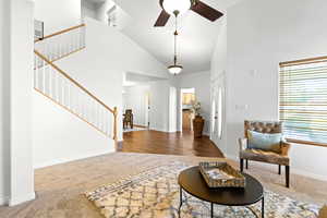 Foyer with ceiling fan, high vaulted ceiling, carpet flooring, and stairs