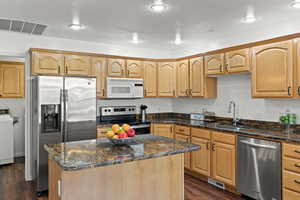 Kitchen with appliances with stainless steel finishes, dark stone counters, visible vents, and a sink