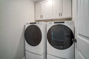 Clothes washing area featuring separate washer and dryer and cabinet space