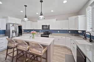 Kitchen with stainless steel appliances, decorative backsplash, white cabinets, and a sink
