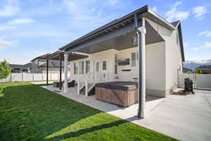 Rear view of property with a fenced backyard, stucco siding, a hot tub, a patio area, and a lawn