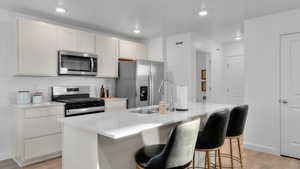 Kitchen featuring stainless steel appliances, light countertops, light wood finished floors, and an island with sink