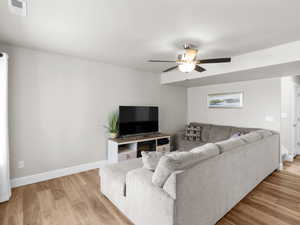 Living room featuring baseboards, visible vents, a ceiling fan, and light wood-style flooring