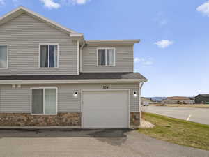 View of side of home with roof with shingles, an attached garage, and stone siding
