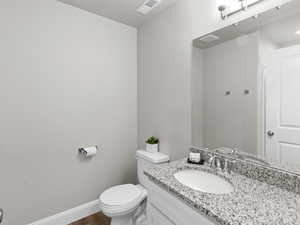 Bathroom featuring vanity, toilet, visible vents, baseboards, and wood finished floors