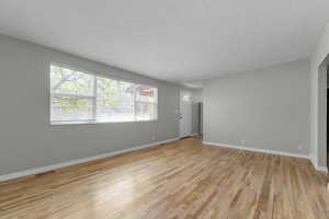 Unfurnished living room featuring a textured ceiling, visible vents, light wood-style flooring, and baseboards