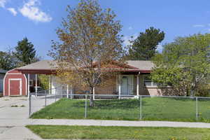 Single story home featuring a fenced front yard, an attached carport, a front lawn, a shed, and concrete driveway