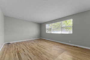 Unfurnished room with a textured ceiling, visible vents, light wood-type flooring, and baseboards