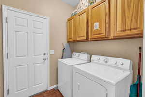 Clothes washing area featuring dark tile patterned floors, washer and dryer, cabinet space, and baseboards