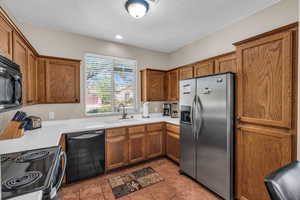 Kitchen with tile patterned floors, light countertops, brown cabinets, black appliances, and a sink