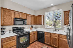 Kitchen featuring light tile patterned floors, black appliances, a sink, and brown cabinets