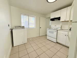 Kitchen with under cabinet range hood, white appliances, washer / clothes dryer, baseboards, and white cabinets