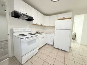 Kitchen with a sink, under cabinet range hood, white appliances, white cabinetry, and light countertops