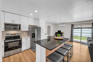Kitchen featuring white cabinetry, a wall mounted air conditioner, stainless steel appliances, and light wood finished floors