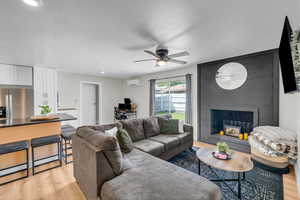 Living room with light wood-type flooring, ceiling fan, a fireplace, and a wall mounted AC