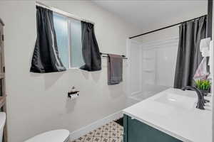 Bathroom featuring baseboards, walk in shower, toilet, tile patterned floors, and vanity