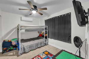 Carpeted bedroom with an AC wall unit, a ceiling fan, and baseboards