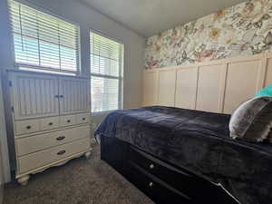 Bedroom with dark colored carpet, wainscoting, a decorative wall, and wallpapered walls
