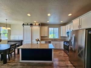 Kitchen with a kitchen island, a barn door, white cabinetry, a sink, and appliances with stainless steel finishes