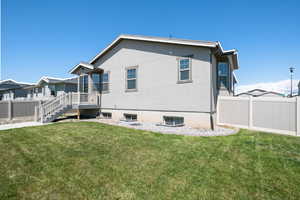 Rear view of house featuring a lawn, central AC, fence, and stucco siding