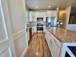 Kitchen with a sink, wood-type flooring, stone countertops, stainless steel appliances, and white cabinetry