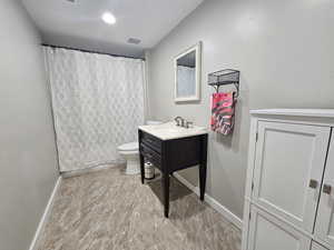 Bathroom featuring a shower with curtain, visible vents, baseboards, vanity, and toilet