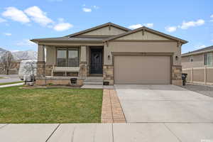 View of front of house with a garage, a front lawn, stone siding, board and batten siding, and concrete driveway