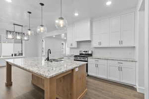 Kitchen featuring a sink, decorative backsplash, stainless steel range with gas cooktop, white cabinets, and dark wood finished floors