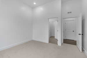 Unfurnished bedroom featuring recessed lighting, carpet flooring, baseboards, visible vents, and a towering ceiling