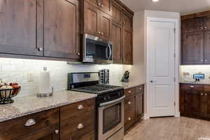 Kitchen featuring light stone counters, stainless steel appliances, decorative backsplash, and dark brown cabinets