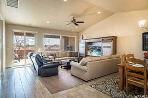 Living room featuring visible vents, vaulted ceiling, wood finished floors, and ceiling fan with notable chandelier