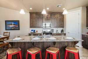 Kitchen featuring tasteful backsplash, dark brown cabinetry, a breakfast bar, visible vents, and appliances with stainless steel finishes