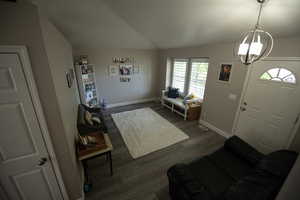 Foyer with an inviting chandelier, vaulted ceiling, dark wood-style flooring, and a healthy amount of sunlight