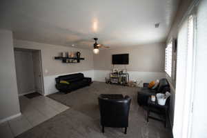 Tiled living room featuring carpet flooring, ceiling fan, a textured ceiling, a wainscoted wall, and visible vents