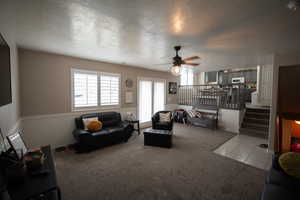 Living area with a ceiling fan, a textured ceiling, wainscoting, light carpet, and stairs