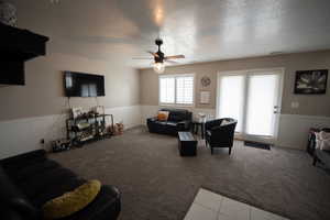 Living room with carpet floors, a ceiling fan, a textured ceiling, and a wainscoted wall