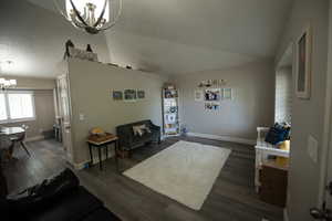 Interior space featuring baseboards, an inviting chandelier, dark wood-style floors, and lofted ceiling